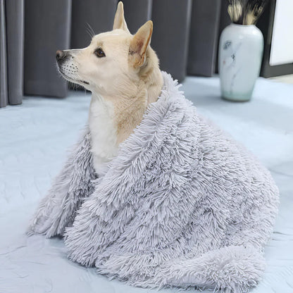 A dog is sitting on a gray fluffy pet blanket, which is draped over the dog.